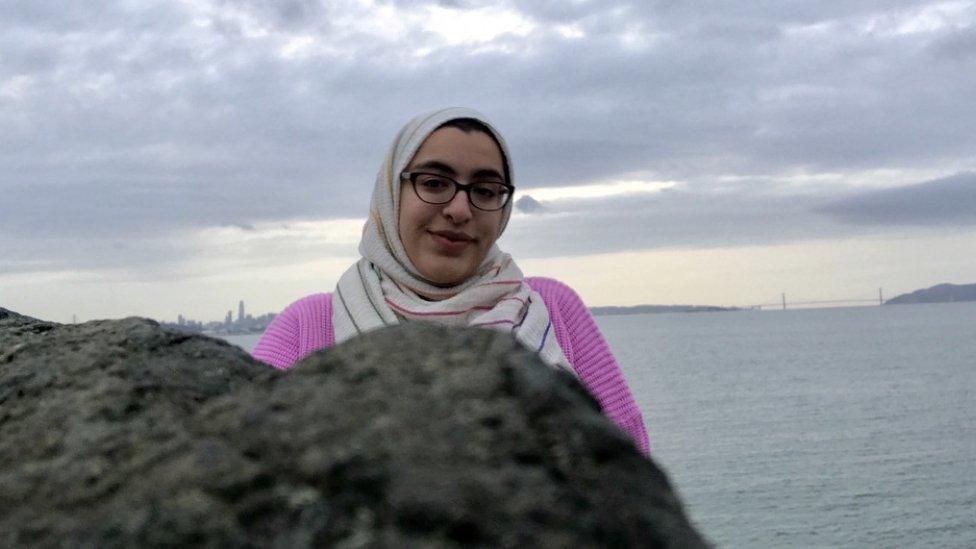 Image of Sabreen Imtair standing in front of the sea in front of a large rock