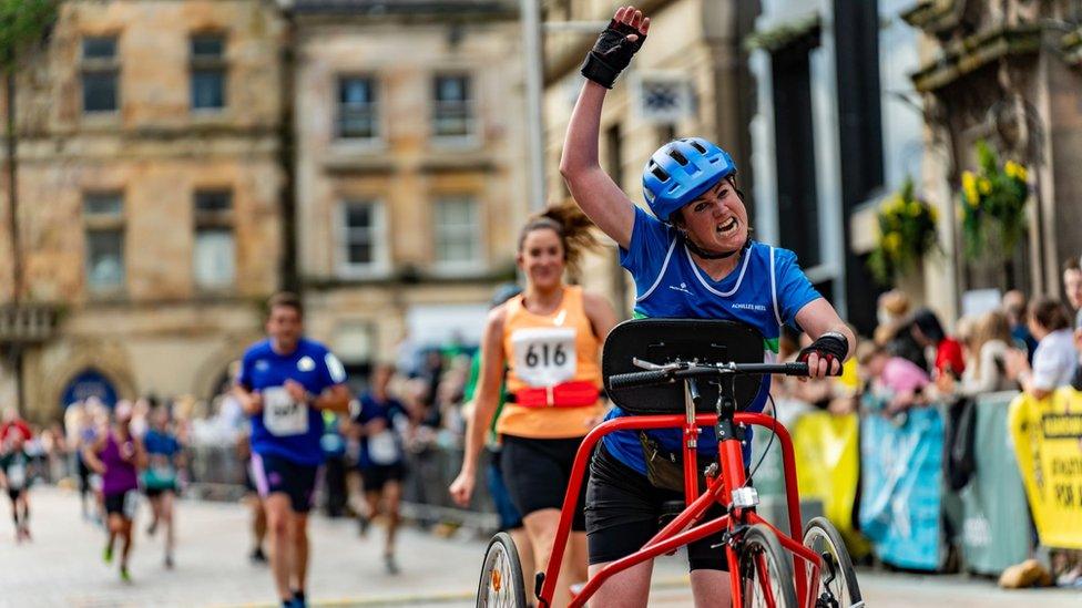 Julie McElroy crossing the finish line of Paisley 10k on frame runner with fist raised in the air