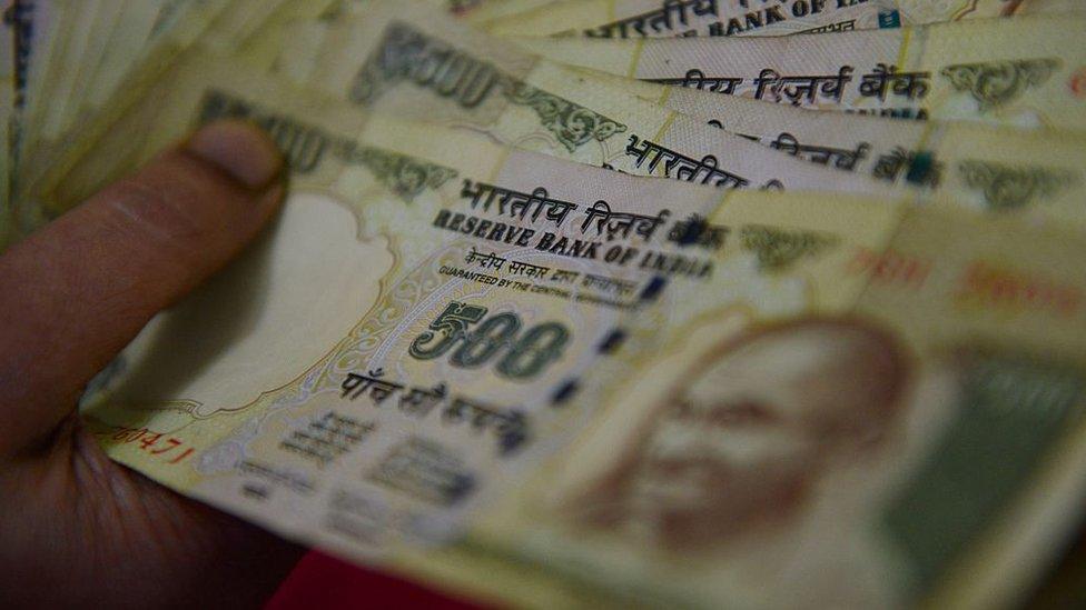 A person holds a wad of 500 rupee notes