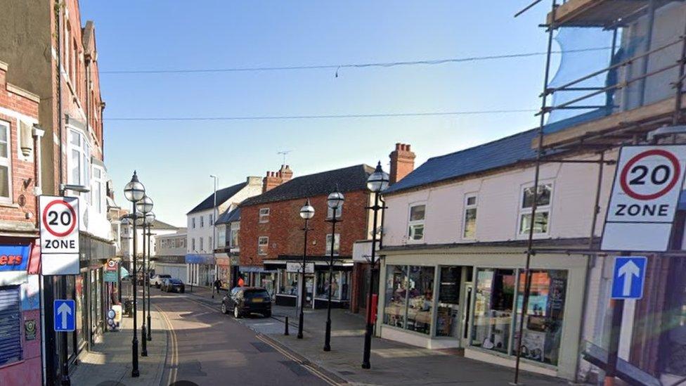 Narrow shopping street with a variety of shops and 20MPH signs