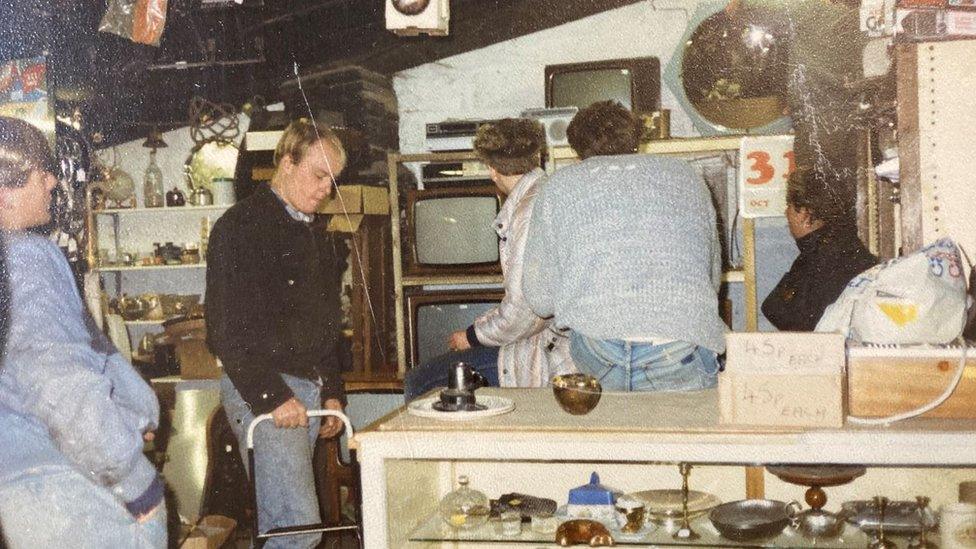 Old photo of five men stood behind the counter in Wot Not, surrounded by antiques