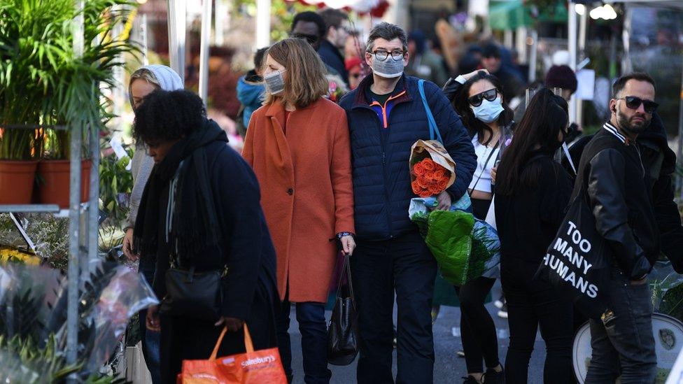 Shoppers wearing a protective face masks visit Columbia Road flower market in east London on Mother"s Day, March 22, 2020. - Up to 1.5 million vulnerable people in Britain, identified as being most at risk from the coronavirus epidemic, should stay at home for at least 12 weeks, the government said Sunday