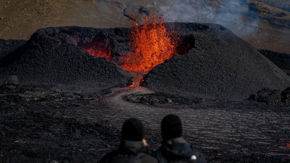 Tourists visit a heart shaped crater as lava flows from the volcano in Fagradalsfjall, Iceland,