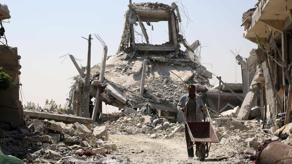 A Syrian man pushes a wheelbarrow past collapsed buildings in the northern Syrian town of Manbij (14 August 2016)