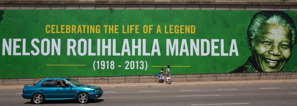 People walk past a giant poster of Nelson Mandela as the former South African president lies in state for a final day at Union Buildings on December 13, 2013 in Pretoria, South Africa.