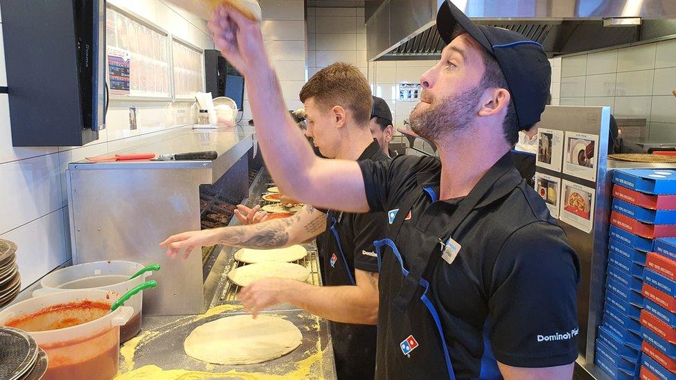 A Domino's Pizza cook flips dough in the air