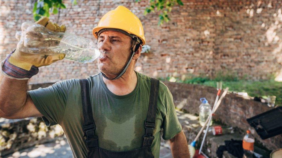 Construction worker who is very hot and drinking water