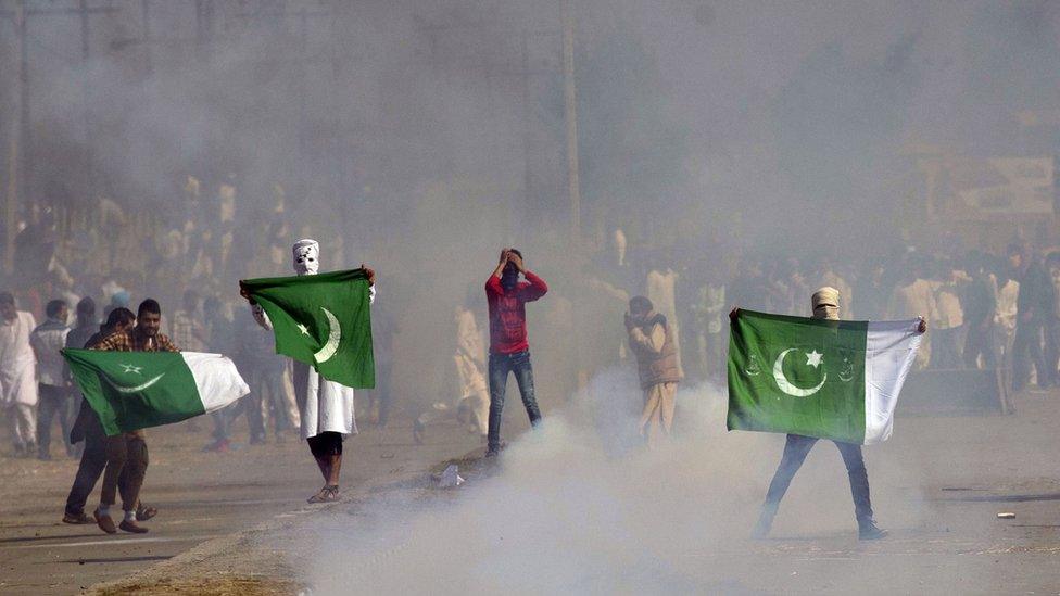 Masked Kashmiris hold the national flag of Pakistan during a protest outside Eidgha, a prayer ground, in Srinagar, Indian controlled Kashmir