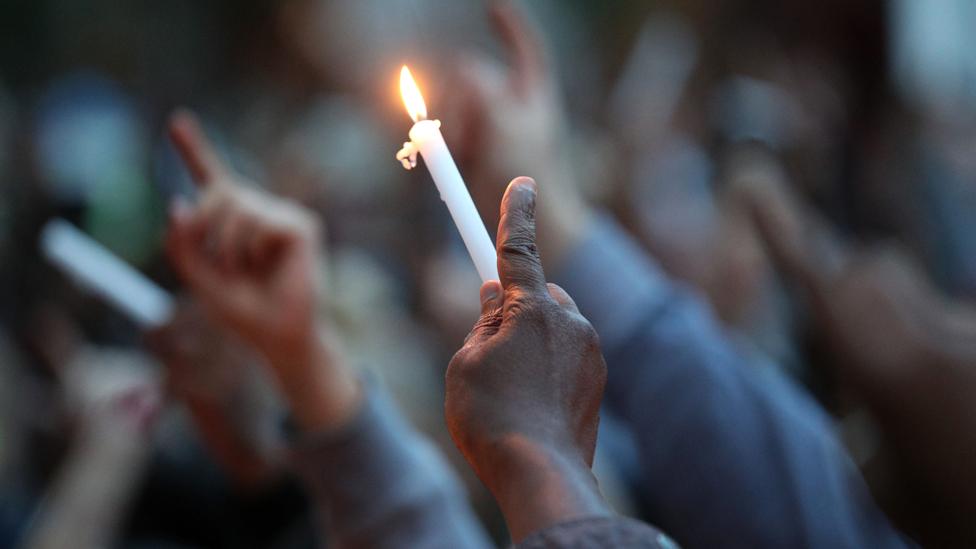 Hand holds lit candle up in vigil to mark four weeks since the disaster