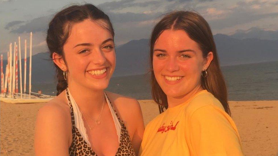 Two young women with auburn hair, smiling on a beach hugging each other