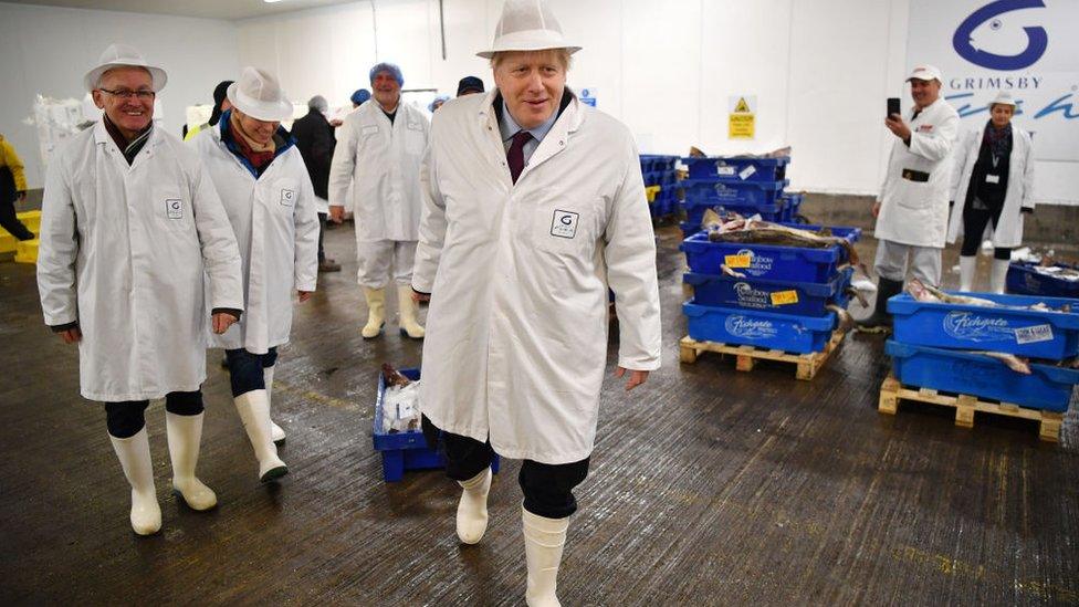 Boris Johnson drags a box of cod along the floor during an election campaign visit to Grimsby Fish Market