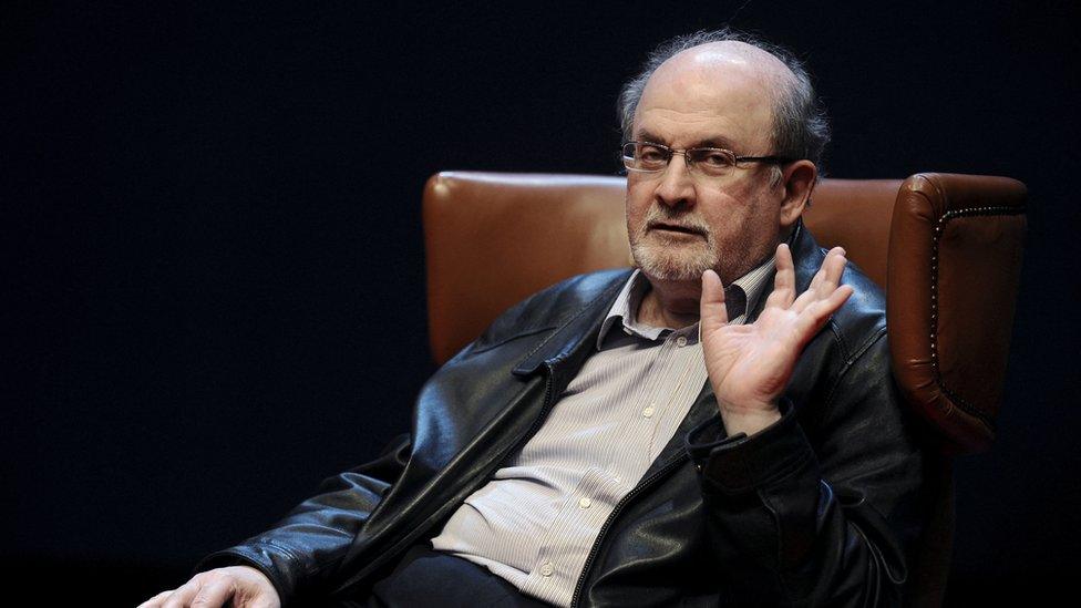 Author Salman Rushdie is seen gesturing while sat in a high leather chair onstage at a launch of one of his books