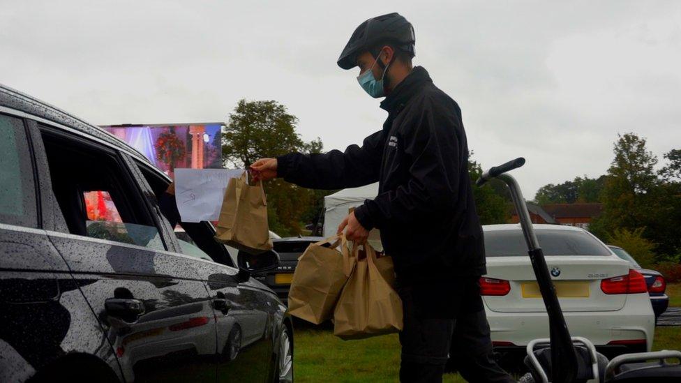 A man passes a bag of snacks through a car window.