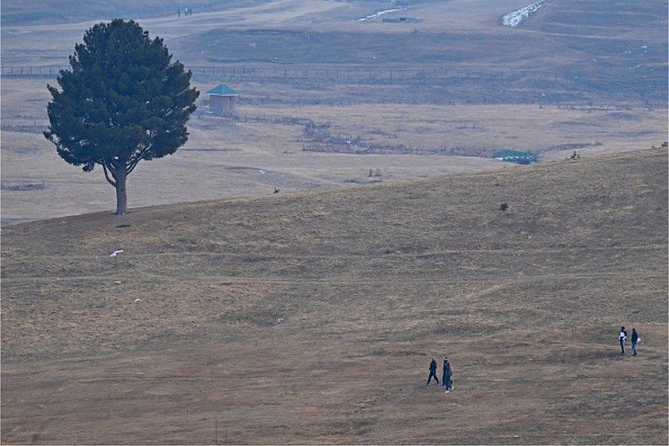 n this photograph taken on January 17, 2024, visitors walk along ski slopes usually covered in snow at this time of the year at a ski station in Gulmarg, some 55 km from Indian-administered Kashmir's capital Srinagar.