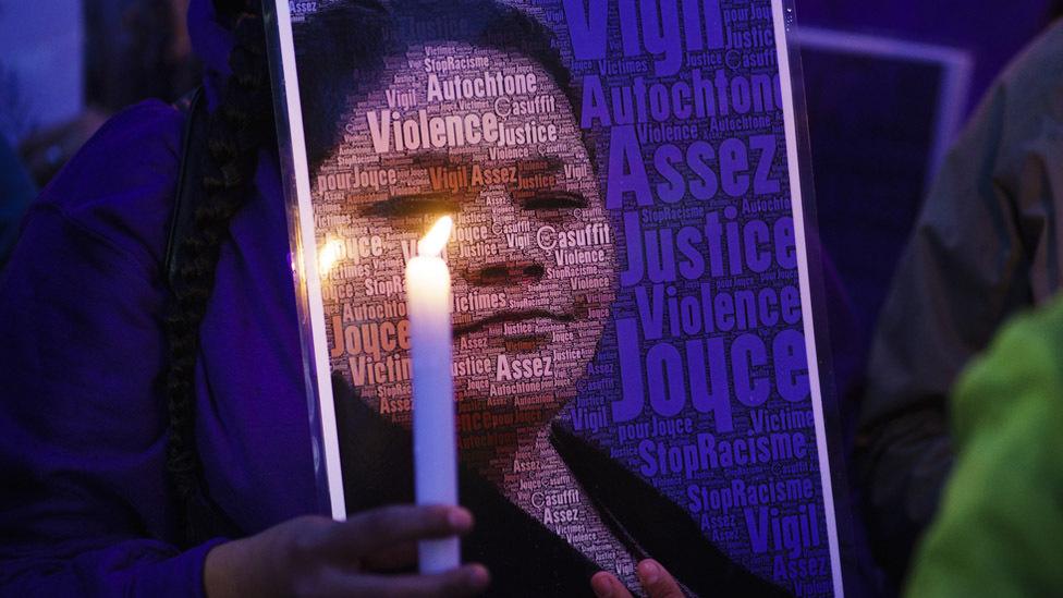 A woman at a vigil holds a candle in front of an image of Joyce Echaquan