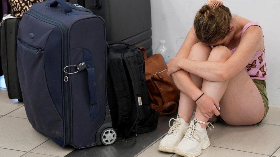 Woman sits next to suitcase at Rhodes airport