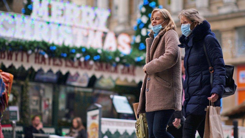 Two women wearing masks walk in Cardiff in front of a Merry Christmas sign