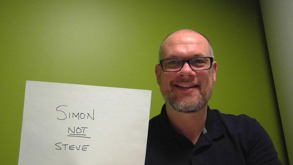 Simon Hewett holds up a sign saying "Simon not Steve"