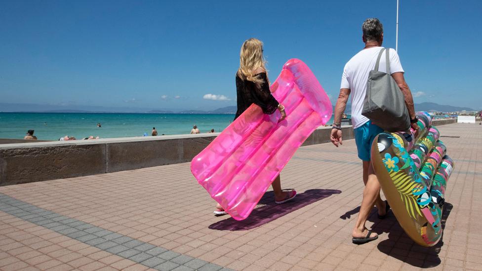 Tourists walk holding inflatable mattress at Palma Beach in Palma de Mallorca on June 7, 2021.