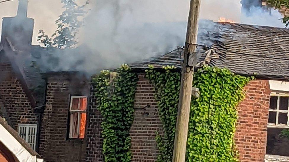 Smoke rises from Ford Green House, with flames behind a top-floor window