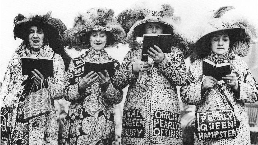 Black and white picture of four women wearing black coats covered in white pearl buttons