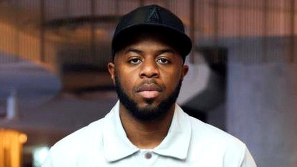 Aaron standing outside, wearing a cap and looking serious