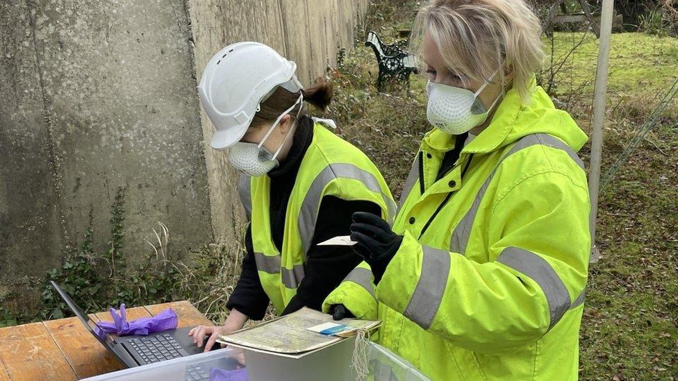 Staff in hi-vis recording items on laptop