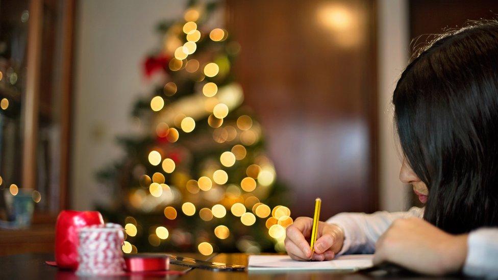 Child writing in front of Christmas tree