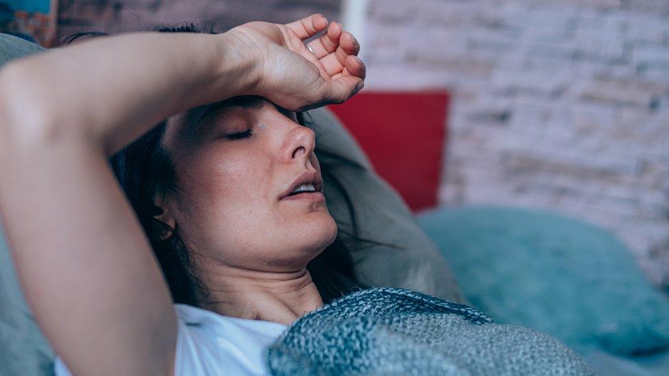 A young woman lies in bed with her hand on her forehead