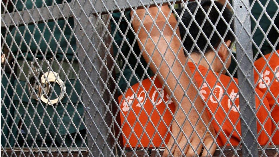 Cambodian Oeuth Ang, in prison uniform and facing away from the camera, behind the a police van wire mesh, outside court in Phnom Penh, Cambodia, 23 March 2017.