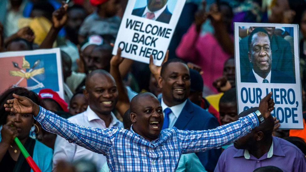 Supporters hold banner, wave Zimbabwean national flag and cheer as they gather to welcome Zimbabwe"s incoming President Emmerson Mnangagwa upon his arrival at Zimbabwe"s ruling Zanu-PF party headquarters in Harare on November 22, 2017.