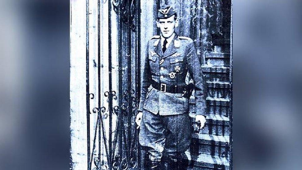 Decorated Luftwaffe pilot Güenter Brixius walks down some steps and through a gate in full uniform