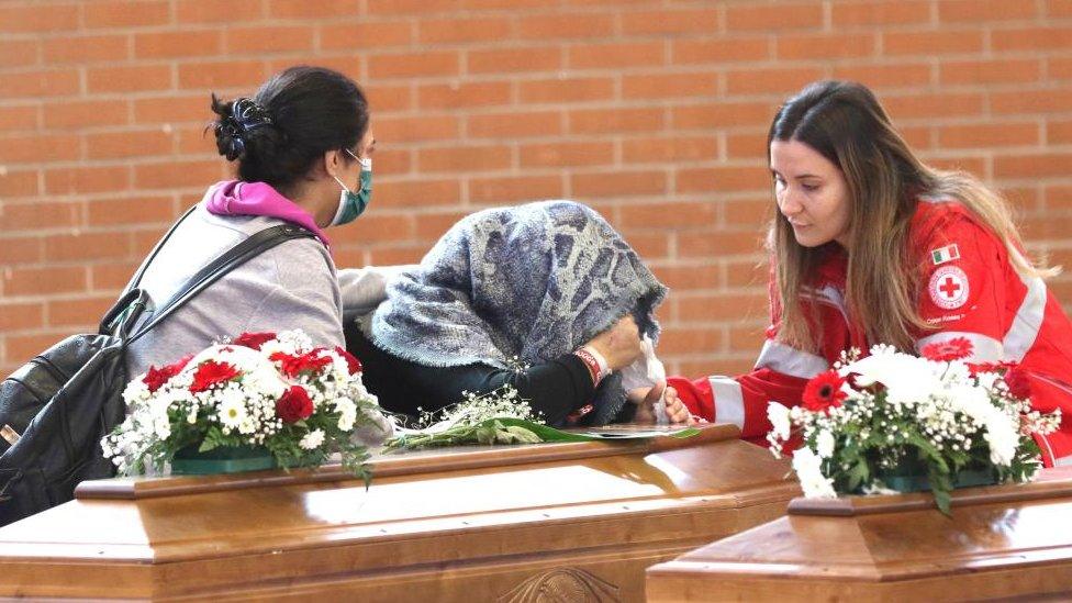 A mourner bends her head over a coffin as two other women watch on