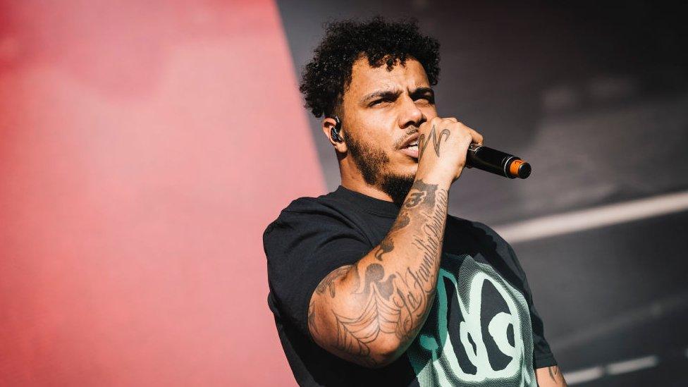 AJ Tracey performing at Laneway festival, he is wearing a black t-shirt and holding a microphone