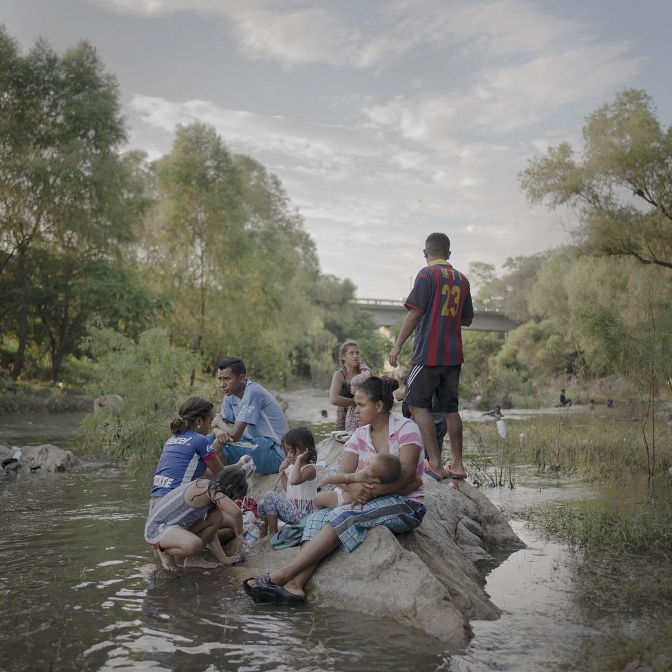 A family sit on a rock in a stream