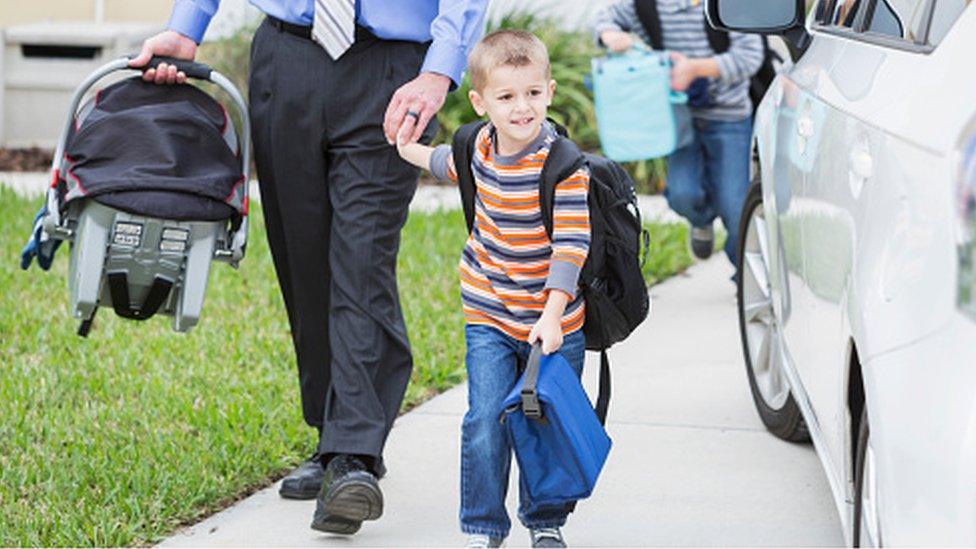 Father carries car seat with small boy holding his other hand