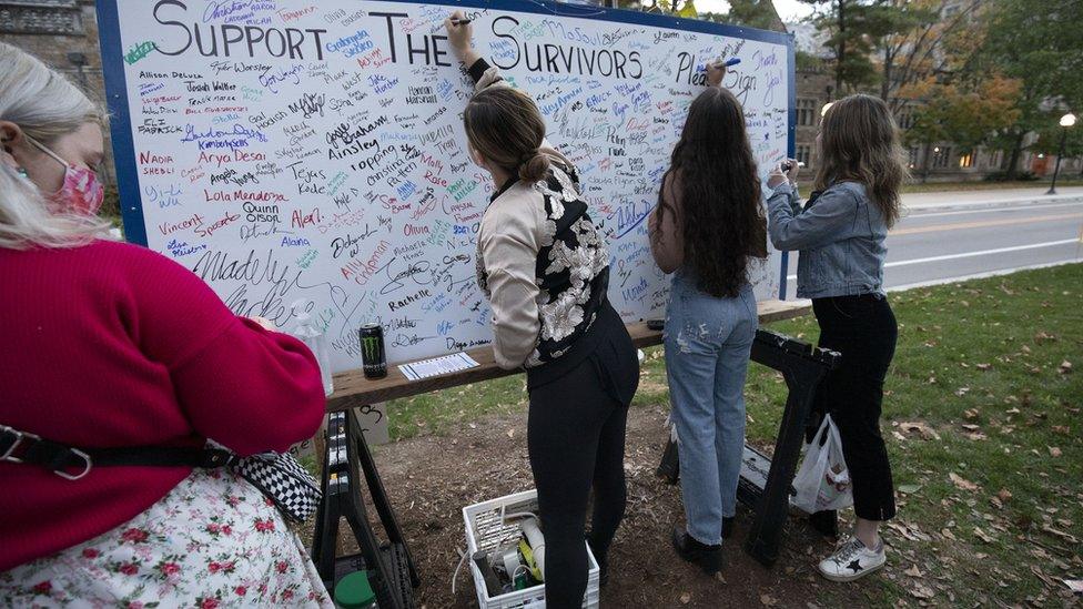 Attendees add their signatures to a board in support of survivors of sexual abuse at a vigil outside the home of outgoing University of Michigan President Mark Schlissel October 13, 2021 in Ann Arbor, Michigan