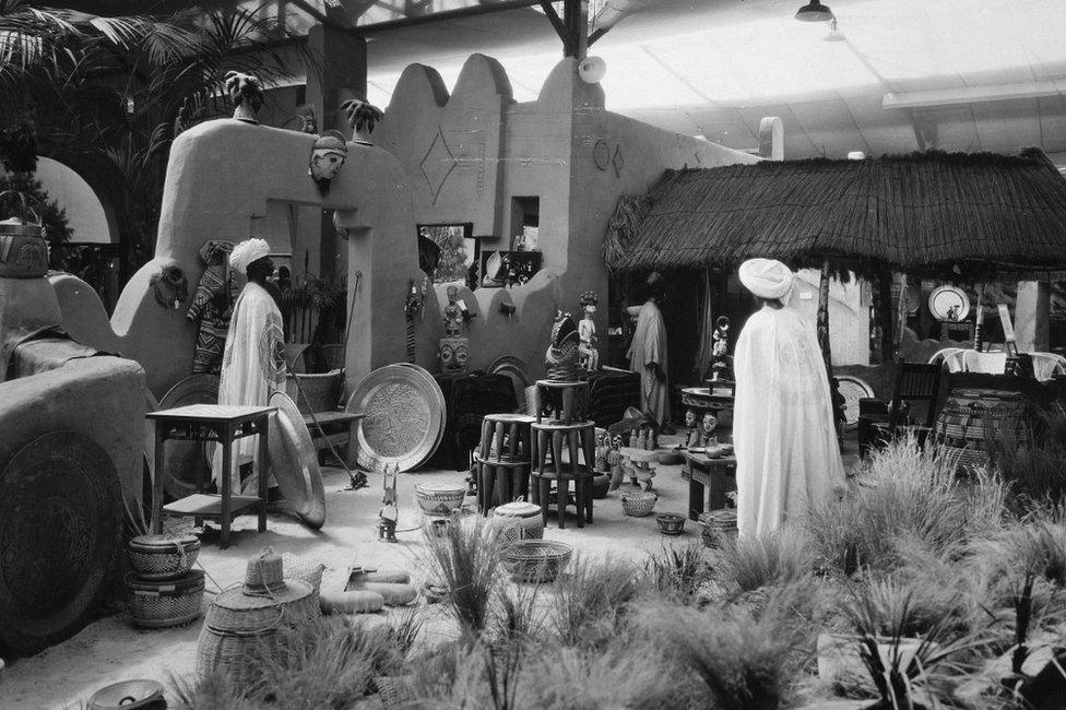 Black and white image of artefacts in West Africa pavilion including models of people