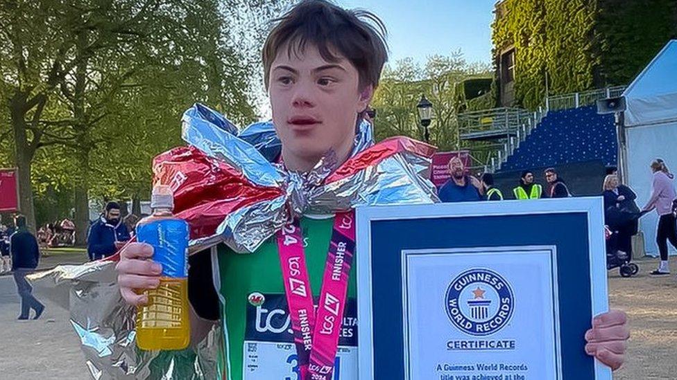 Lloyd holding in is running gear with a welsh flag around his shoulders, a medal and a world record certificate