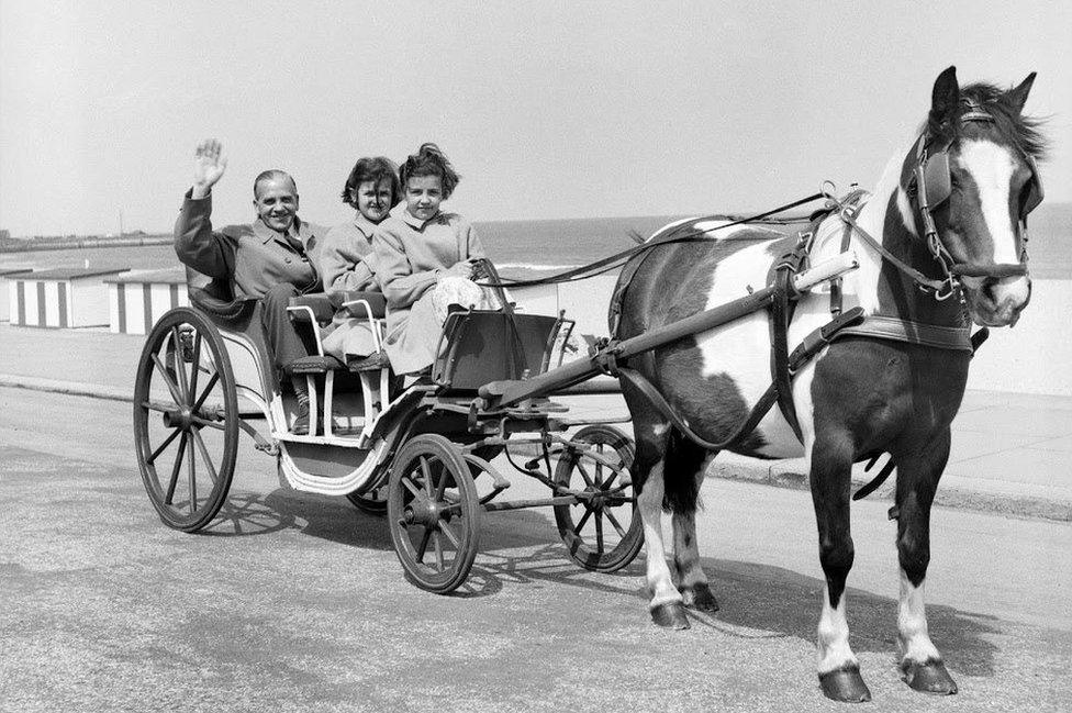 man with two girls in horse-drawn carriage