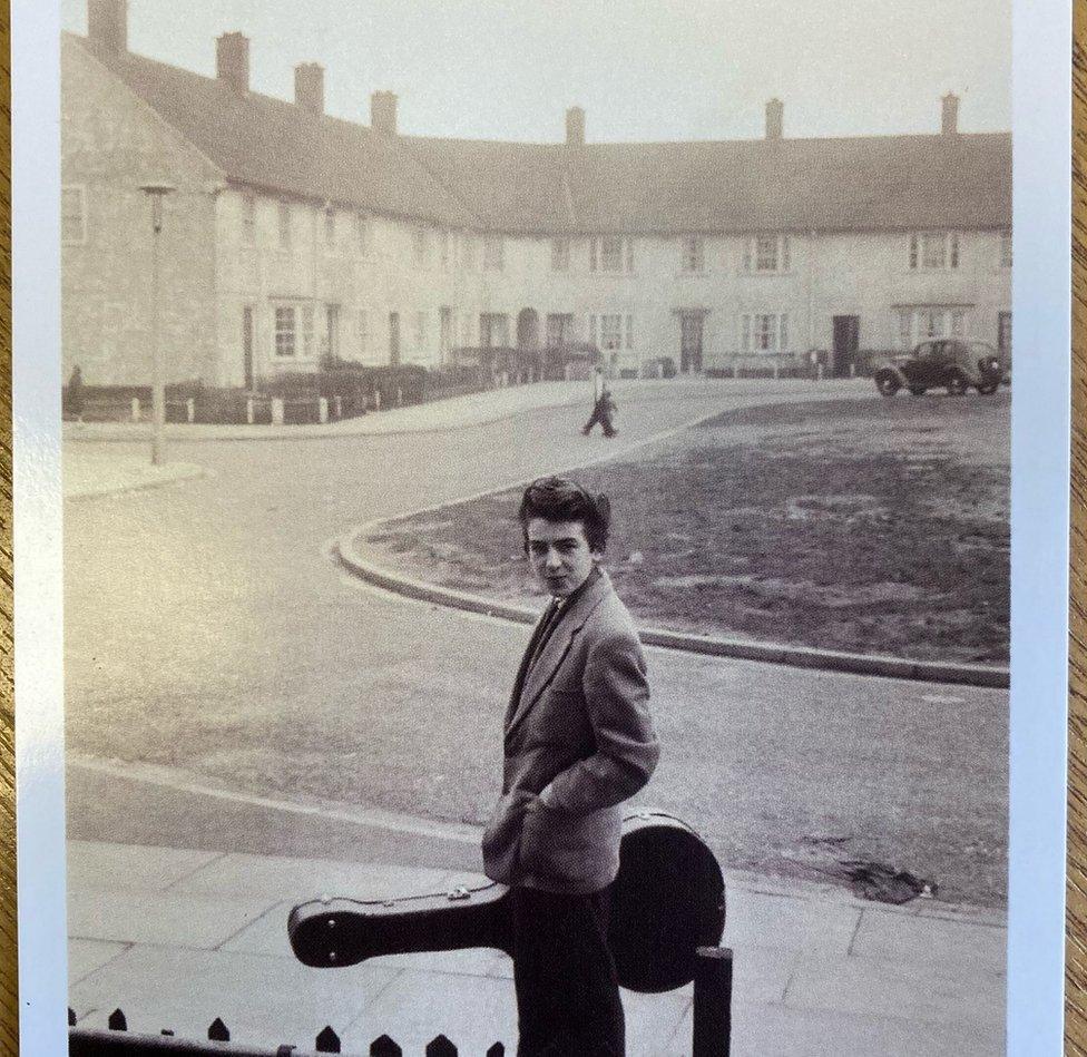 A young George Harrison holding a guitar case outside his Speke home