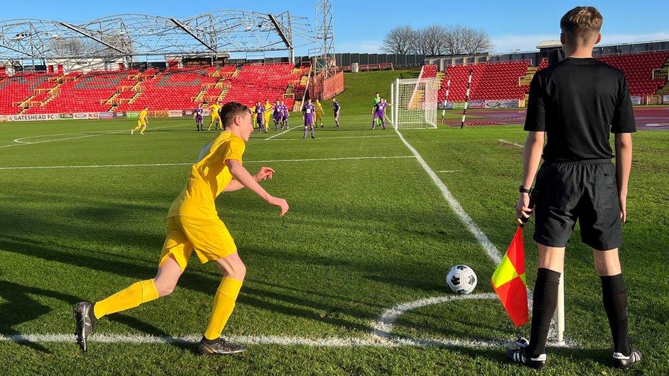 A player in yellow kit runs up to kick a ball from the corner of the pitch