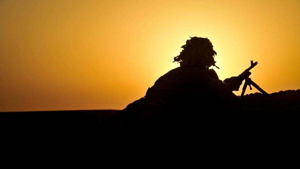 Silhouette of a soldier covering with a gun by a ridge