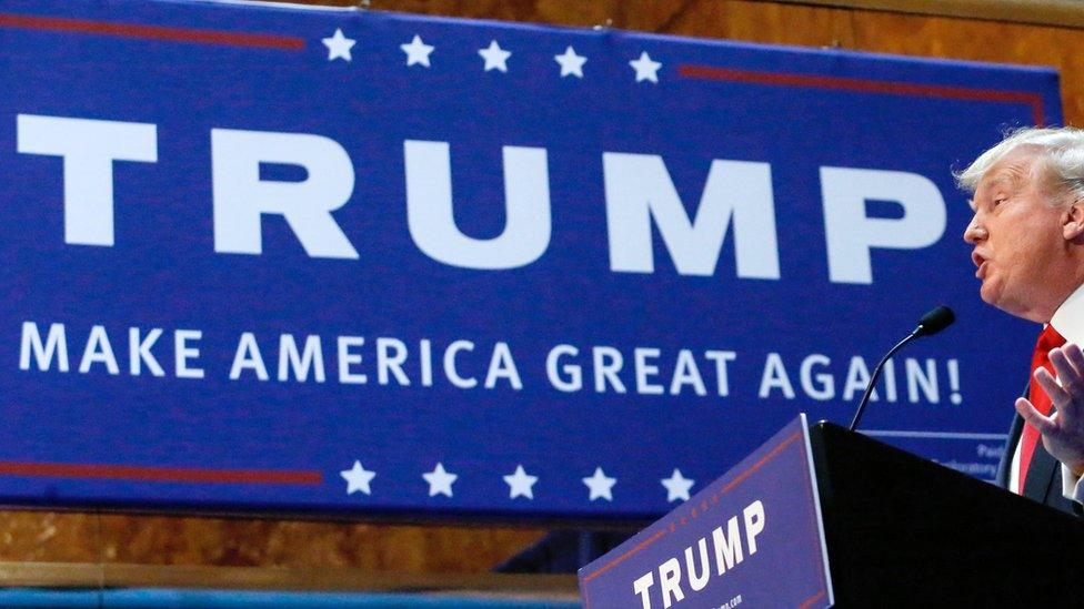 Donald Trump speaks in front of a "Make America Great Again" campaign sign.