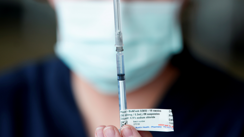 A health worker holds up a needle of the Pfizer vaccine