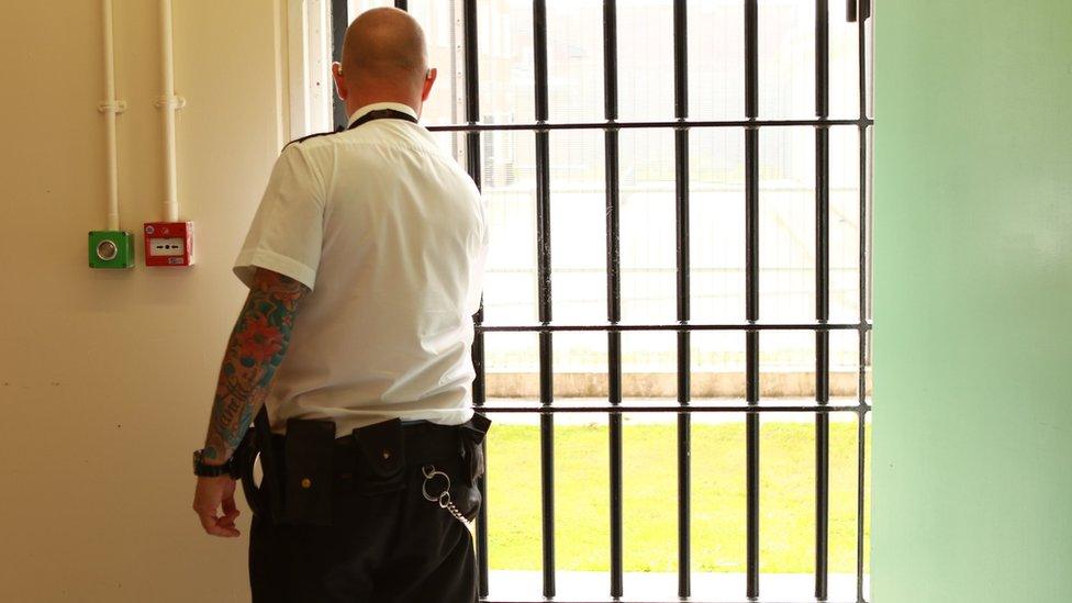 A prison officer closing a metal grid gate