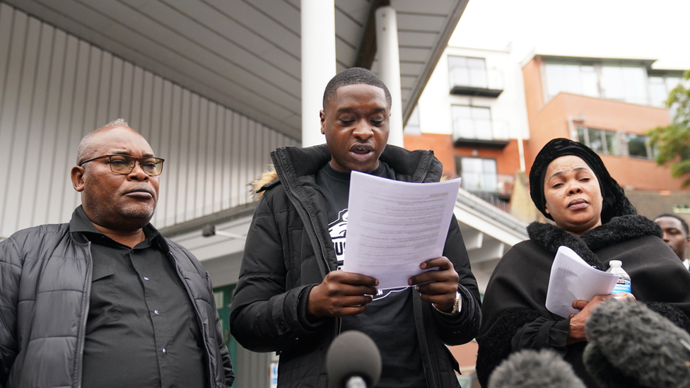 Chris Kaba's cousin Jefferson Bosela reads a statement alongside Chris's parents Prosper Kaba (left) and Helen Lumuanganu