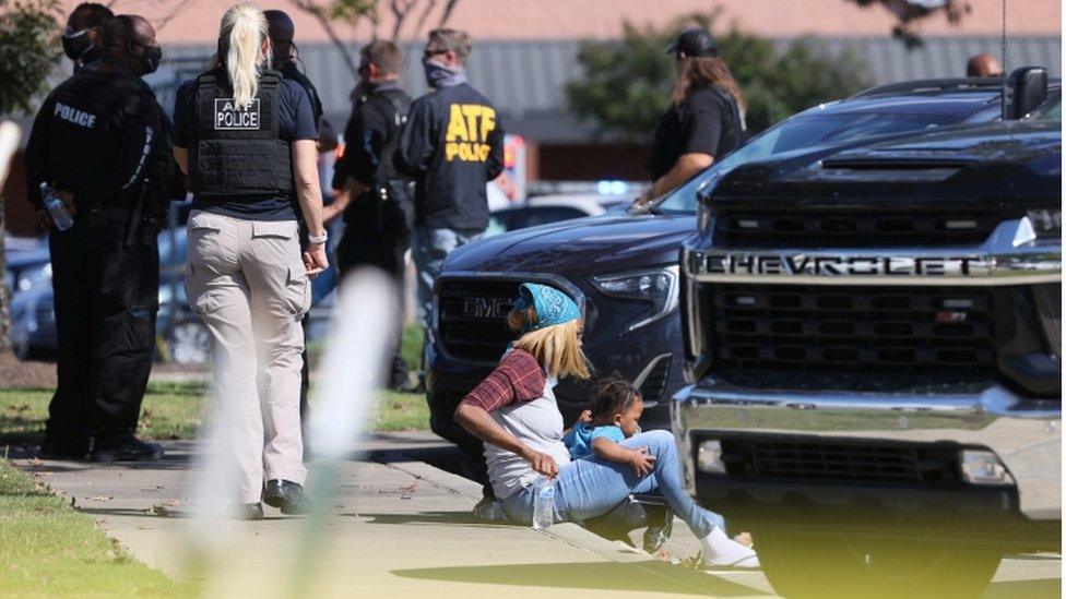 A woman and child rest outside the supermarket crime scene