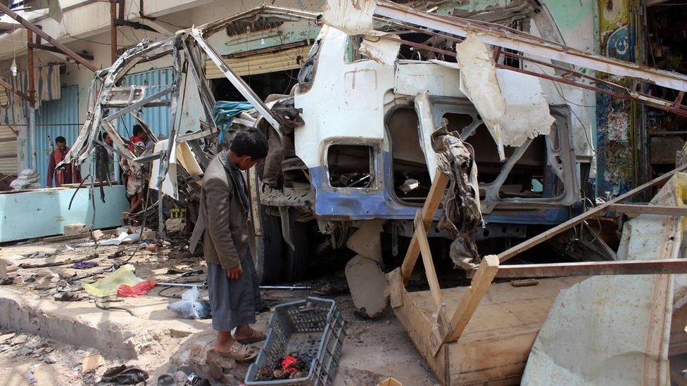 A Yemeni child stands next to the destroyed bus at the site of a Saudi-led coalition air strike, August 2018