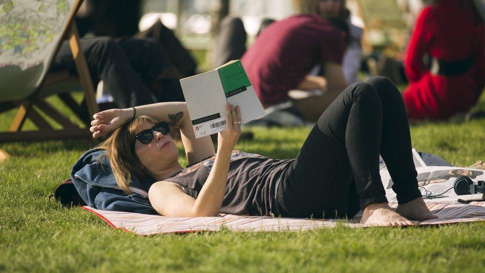 Woman lying on grass reading book at Hay Festival